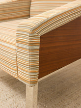 Load image into Gallery viewer, Close-up of a mid-century modern armchair featuring striped upholstery in beige, orange, and brown, with a dark wood side panel and a light-colored metal leg.
