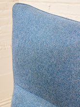Load image into Gallery viewer, A close-up of a blue textured fabric cushion or upholstered furniture corner against a white brick wall background.
