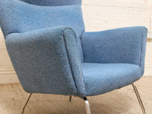 Load image into Gallery viewer, A mid-century modern armchair upholstered in textured blue fabric, featuring a high back, wide armrests, and slim chrome legs, set against a white brick wall and light beige floor.
