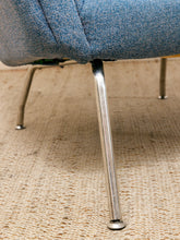 Load image into Gallery viewer, Close-up of a blue upholstered chair leg with a polished metal pedestal base, resting on a beige woven rug.
