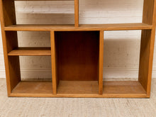 Load image into Gallery viewer, A mid-century modern wooden open shelving unit with multiple cubby compartments, shown against a white brick wall and light beige rug.
