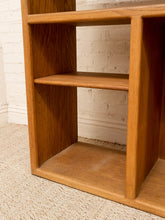 Load image into Gallery viewer, A close-up of a wooden bookshelf with three shelves, made of medium brown wood, set against a white brick wall and beige carpet.
