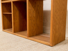 Load image into Gallery viewer, A close-up of a wooden shelving unit with open cubbies, showing a warm medium-brown wood grain finish, set on a beige textured carpet against a white brick wall.
