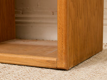 Load image into Gallery viewer, Close-up of the corner joint and bottom edge of a light oak wood furniture piece, showing the natural wood grain and a crack on the front apron, set on a beige woven rug.
