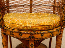 Load image into Gallery viewer, A close-up of a round, plush cushion with a yellow and orange paisley pattern, resting on a woven rattan chair.
