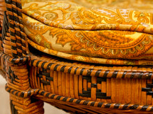 Load image into Gallery viewer, Close-up of a woven rattan chair with a thick cushion upholstered in a warm yellow and orange paisley fabric.
