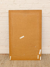 Load image into Gallery viewer, The back of a large square canvas or framed print, secured with white tape, leaning against a white painted brick wall on a woven rug.

