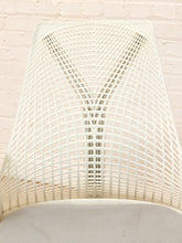 Load image into Gallery viewer, A close-up of a white slatted plastic chair backrest, showing the curved grid pattern against a white painted brick wall background.
