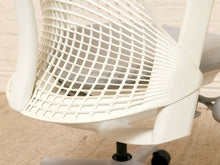 Load image into Gallery viewer, Close-up of a modern ergonomic office chair with a white curved mesh backrest and white plastic frame, showing part of the base and casters.
