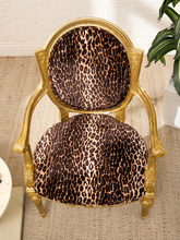 Load image into Gallery viewer, An ornate gold-framed accent chair with plush leopard-print upholstery on the seat and backrest, set on a woven jute rug next to a potted plant.
