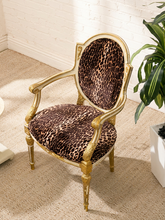 Load image into Gallery viewer, An ornate accent chair with a gold gilded frame and brown leopard-print upholstered seat and backrest, set on a beige carpet next to a potted plant.
