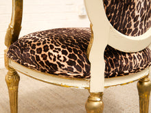 Load image into Gallery viewer, Close-up of an upholstered chair with a leopard-print fabric seat cushion and backrest, set on a distressed gold and cream painted frame.
