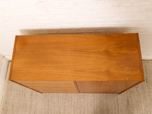 Load image into Gallery viewer, A mid-century modern wooden sideboard cabinet with a warm honey-toned wood grain finish, photographed from a high angle against a white brick wall and textured rug.
