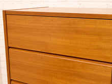 Load image into Gallery viewer, Close-up of a mid-century modern wooden chest of drawers with warm honey-toned teak wood grain, featuring two visible drawers and a white brick wall background.
