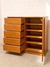 Load image into Gallery viewer, A mid-century modern wooden storage cabinet with five drawers on the left and an open shelving compartment on the right, set against a white brick wall and beige carpet.
