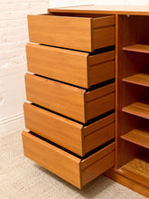 Load image into Gallery viewer, A mid-century modern wooden chest of drawers with five open drawers on the left and open shelving on the right, made of warm medium-brown wood grain, set against a white brick wall and beige carpet.
