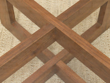 Load image into Gallery viewer, Close-up of a wooden table base with intersecting crossed legs in a medium warm brown finish, resting on a woven beige rug.
