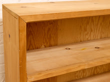 Load image into Gallery viewer, Close-up of a light natural wood bookshelf with a single open shelf, showing the wood grain and knots, set against a white brick wall.
