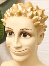 Load image into Gallery viewer, A close-up of a mannequin or display bust with a sculpted spiky blond wig, beige skin, and dark brown eyes, shown against a softly blurred indoor background.
