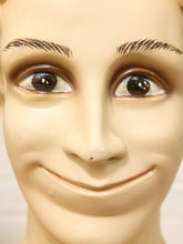 Load image into Gallery viewer, A close-up of a beige mannequin or doll face with brown eyebrows, realistic brown eyes, and a small smile, photographed against a light neutral background.
