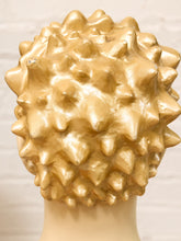 Load image into Gallery viewer, A golden spiky wig displayed on a cream-colored mannequin head against a light brick wall background.

