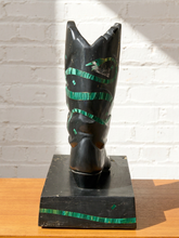 Load image into Gallery viewer, A carved black wooden cowboy boot sculpture with green inlay details, displayed on a black base against a white brick wall.
