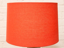 Load image into Gallery viewer, A bright orange fabric drum lampshade with a visible woven texture, shown against a white painted brick wall background.
