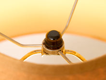 Load image into Gallery viewer, Close-up of a lampshade interior with a central light fixture socket, warm amber-toned fabric, and thin metal support rods.
