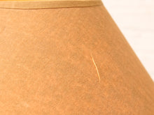 Load image into Gallery viewer, Close-up of a tan or camel-colored fabric lampshade with a visible thin needle or scratch on the front.

