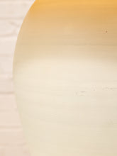 Load image into Gallery viewer, A close-up of a large, rounded object with a warm gradient color transition from golden yellow at the top to cream and light beige at the bottom, set against a light off-white brick wall background.
