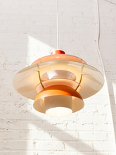Load image into Gallery viewer, A mid-century modern multi-tiered pendant light with translucent amber and warm beige shades, suspended against a white brick wall with soft sunlight casting shadows.
