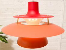 Load image into Gallery viewer, A mid-century modern pendant light with a red top canopy, a wide coral-orange shade, and a smaller orange base, shown against a white brick wall.
