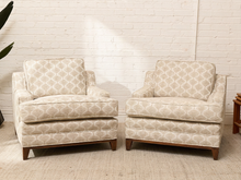 Load image into Gallery viewer, A pair of upholstered armchairs with a beige and white geometric patterned fabric, set against a white brick wall background.
