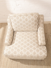 Load image into Gallery viewer, A single upholstered armchair with a cream and beige geometric trellis pattern, positioned on a textured beige rug against a white brick wall.
