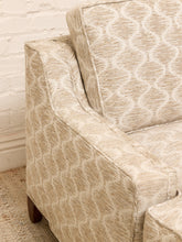 Load image into Gallery viewer, Close-up of a beige upholstered armchair with a cream geometric trellis pattern, set against a white brick wall and light rug.
