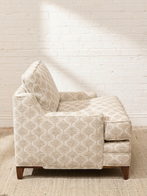Load image into Gallery viewer, A single upholstered accent chair in a light beige fabric with a subtle geometric lattice pattern, shown from the side against a white brick wall and textured rug.
