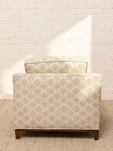 Load image into Gallery viewer, A single upholstered armchair with a light beige and white geometric trellis pattern, shown from the back against a white brick wall on a textured rug.
