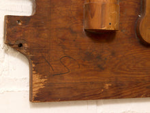 Load image into Gallery viewer, A close-up of a rustic wooden wall-mounted object with a curved lower edge, visible screws, a cylindrical protruding section, and faint handwritten markings on a white painted brick wall.
