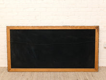 Load image into Gallery viewer, A rectangular black chalkboard with a natural wood frame, leaning against a white painted brick wall on a textured beige carpet.
