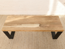 Load image into Gallery viewer, A rustic rectangular wooden coffee table with a natural live-edge top and black metal legs, shown on a textured beige rug against a white brick wall.
