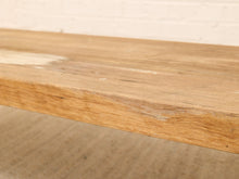 Load image into Gallery viewer, Close-up of a rustic light brown wooden tabletop showing natural wood grain and live edges, set against a white brick wall and neutral floor.

