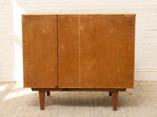 Load image into Gallery viewer, A mid-century modern wooden sideboard cabinet with two doors, shown against a white brick wall and textured beige rug.
