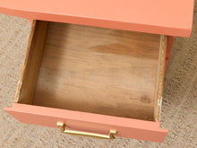 Load image into Gallery viewer, A close-up of a coral pink drawer with its front panel pulled open, revealing a light natural wood interior. The drawer has a brass pull handle and sits on a beige textured rug.
