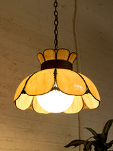 Load image into Gallery viewer, A vintage-style stained glass pendant light with a warm yellow and amber petal design, hanging from a dark metal chain against a white brick wall.

