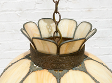 Load image into Gallery viewer, A close-up of a vintage stained glass pendant light, showing cream-colored glass panels with dark gray lead lines and a bronze metal band, suspended by a chain against a white brick wall.
