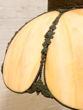 Load image into Gallery viewer, Close-up of a vintage-style stained glass lamp shade with cream-colored glass panels and dark green metal trim, set against a white brick wall background.
