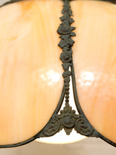 Load image into Gallery viewer, Close-up of a vintage-style table lamp shade featuring a glossy, warm cream-colored glass or shell-like surface divided by an ornate, dark bronze metal central frame with floral and scrollwork details.
