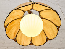 Load image into Gallery viewer, A vintage-style flower-shaped pendant light with amber-tinted glass petals and a central glowing white globe shade, suspended against a white painted brick wall.
