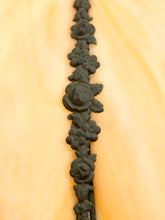 Load image into Gallery viewer, A close-up of a dark cast iron floral rosette border trim running vertically down the center of a light peach-colored wooden surface.
