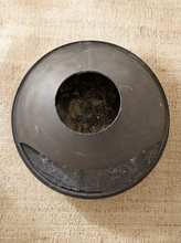 Load image into Gallery viewer, A dark gray circular metal or plastic container with a central hole, photographed from above on a textured beige fabric background.
